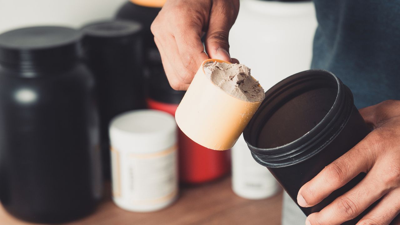 Close up on man&#039;s hand scooping protein powder into flask