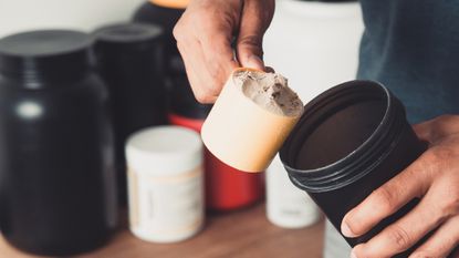 Close up on man's hand scooping protein powder into flask
