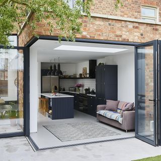 single-storey rear extension containing a black and white kitchen with black bifold doors that cover two walls, leading out to a garden