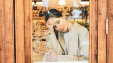 A pensive young woman alone with a glass of champagne looks out of a restaurant window