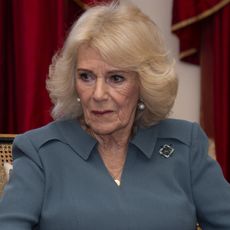 Queen Camilla wears a dark green dress and has blonde coiffed hair and pearl earrings