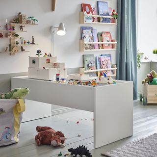 playroom with shelving for books, wall light, desk for toys, white floor, rug, toys, lego