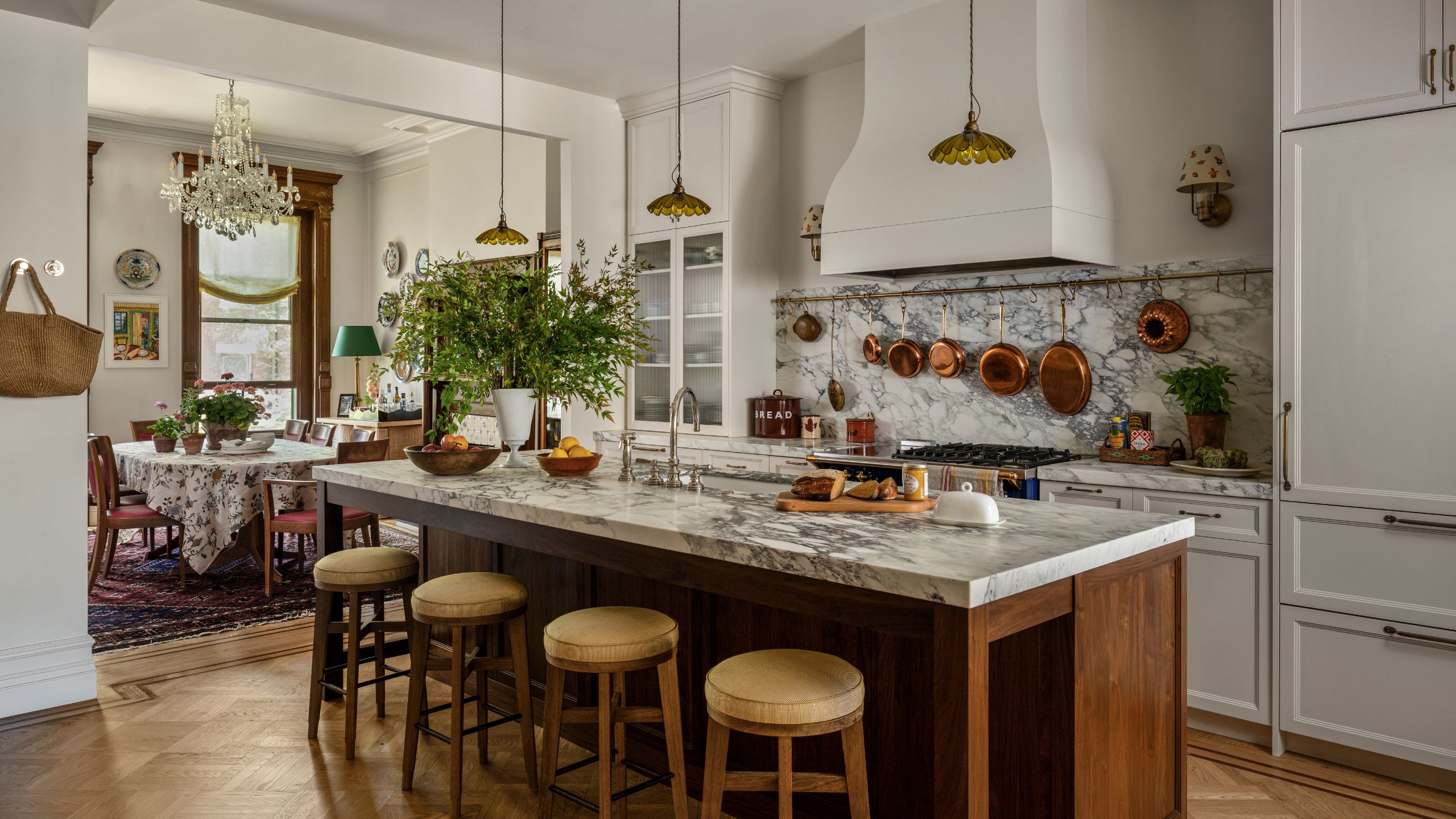 a new york brownstone kitchen with white cabinetry and a wooden island with marble counter and small vintage style pendants