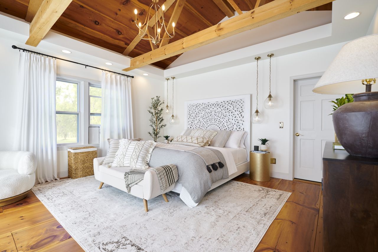 A bedroom with white furnishings and vaulted ceiling with wooden beams