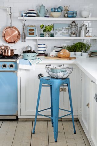 White kitchen with blue range cooker, shabby chic stool and coastal decor on shelves