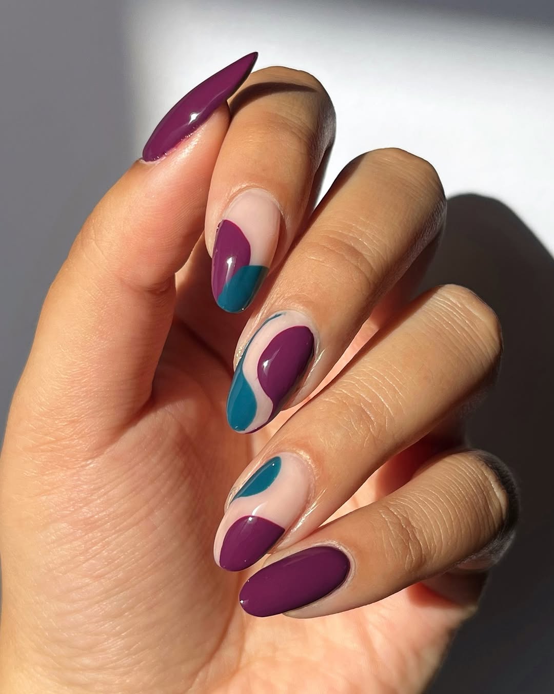 Close-up photo of a person&amp;rsquo;s hand showcasing a purple and teal swirl design manicure on almond nails.
