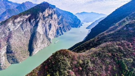 An aerial shot of the Yangtze river, a teal colored strip of water seen between two lush, rocky peaks. 
