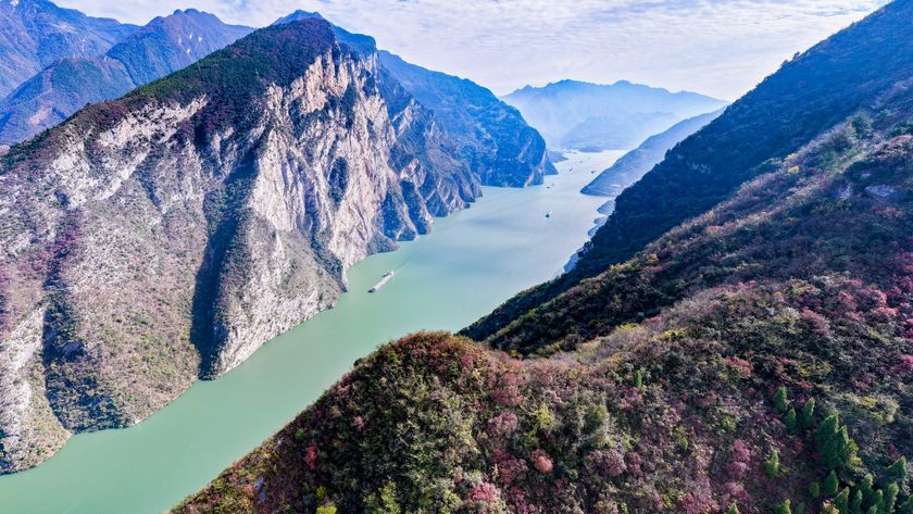 An aerial shot of the Yangtze river, a teal colored strip of water seen between two lush, rocky peaks. 