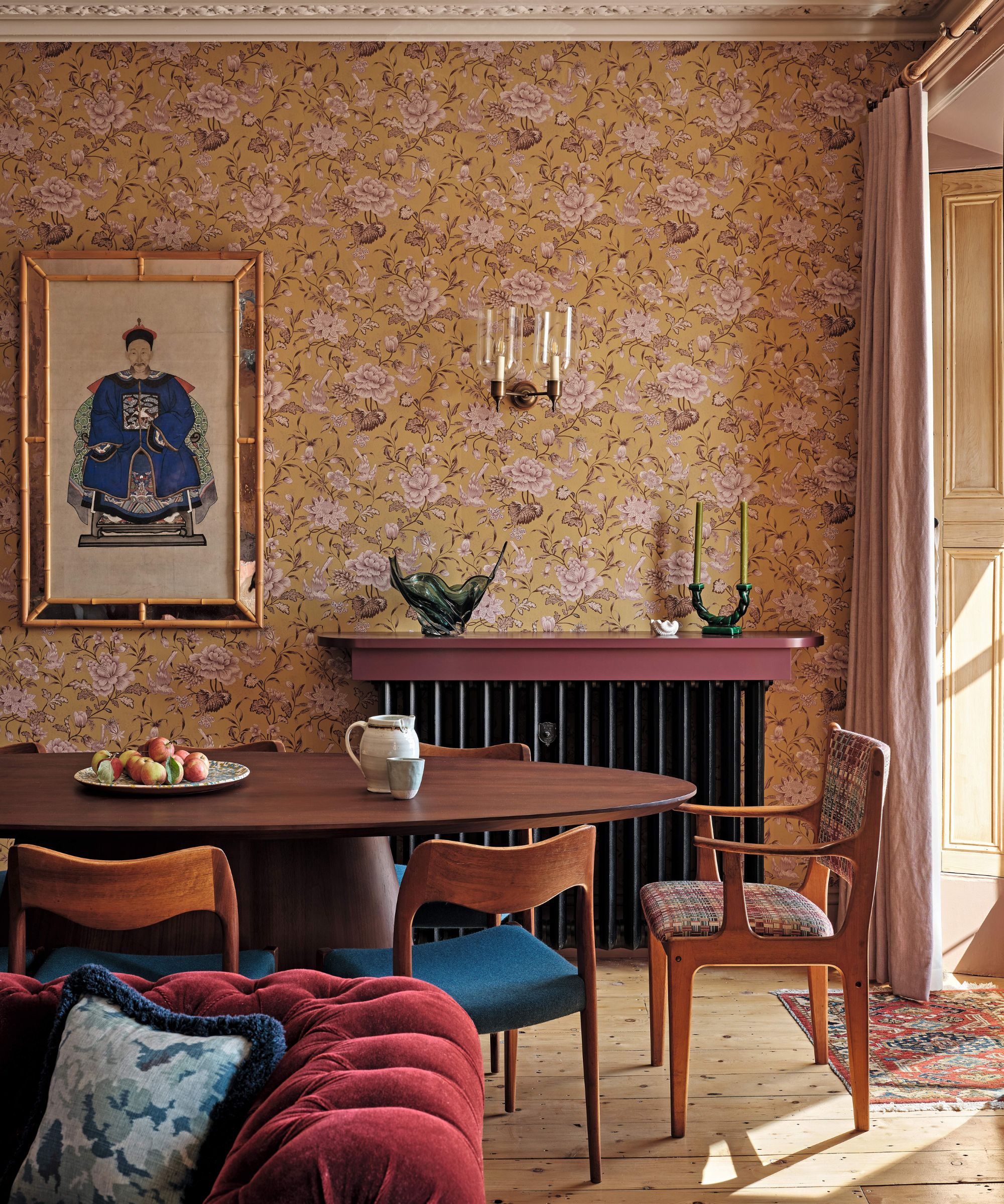 a yellow and pink floral sitting room with dining space, dark red velvet couch and pink window drapes