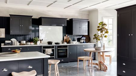 a large black kitchen, with a big island with a marble counter, and a wooden dining area next to the windows