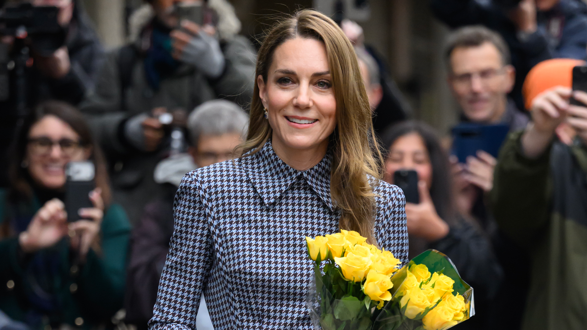 Kate Middleton wearing a checkered dress holding yellow flowers