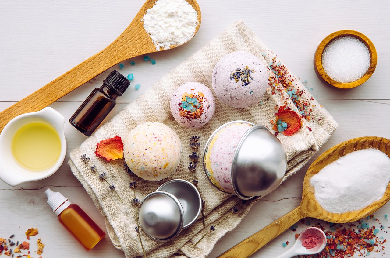 Making bath bombs at home. Iingredients on table on wood spoons cornstarch, essential oil, dye, citric acid, baking soda, dry herbs, round metal pressing molds