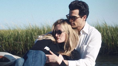 Caroline sits on John's lap with his arms wrapped around her in FX's Love Story