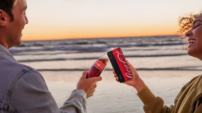 The Realme 10 Pro Coca Cola limited edition, with a glass bottle of coke at sunset, on the beach