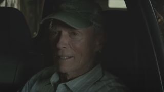 Clint Eastwood in the driver's seat of a car, wearing a cap.