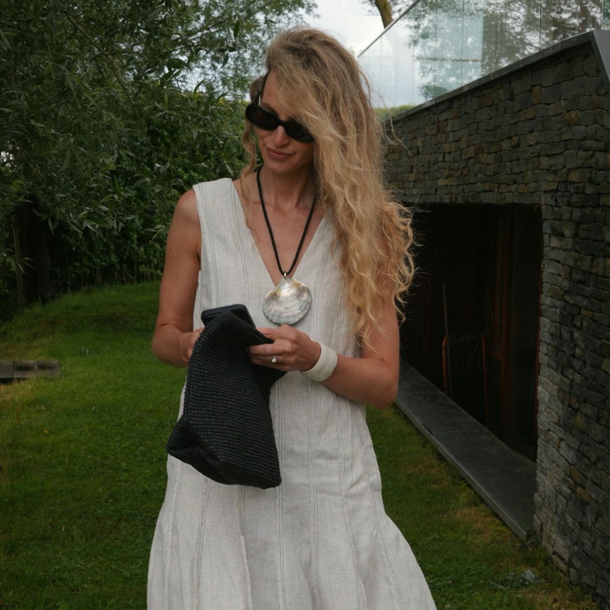 Woman wears sunglasses, dress, shell necklace