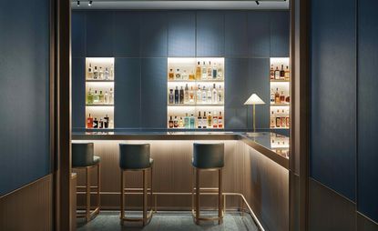 Bar with bar stools and spirit bottles on lit shelves