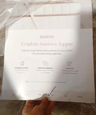 A hand holding the care guide for the Saatva Graphite Mattress Topper.