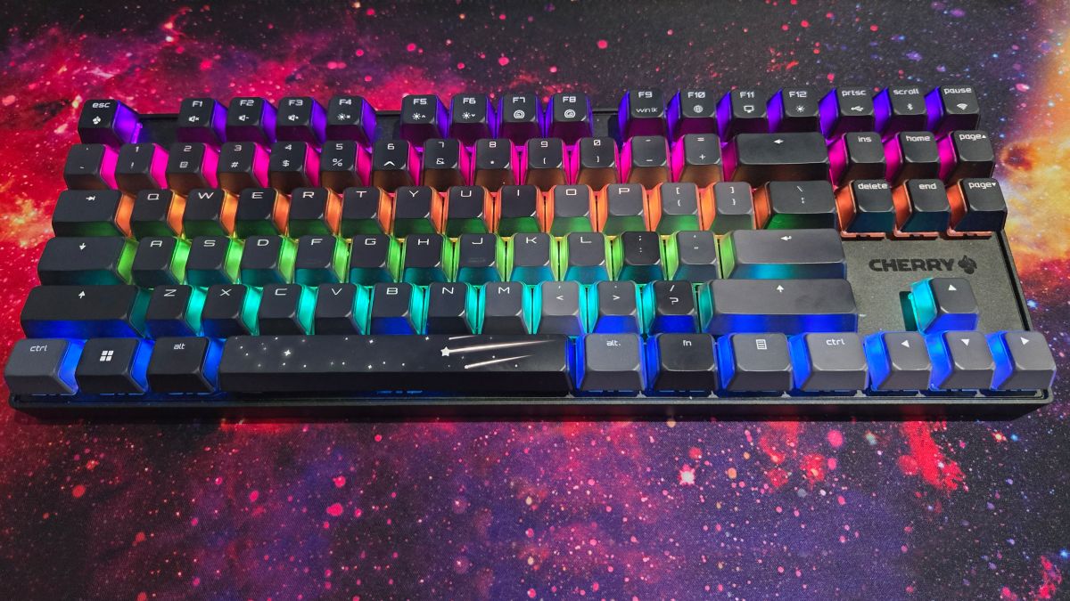 The Cherry MX 8.2 Wireless Xaga gaming keyboard sits on a large mouse mat depicting a nebula. This visual motif ties into the shooting star design on the keyboard&#039;s space bar. The keyboard&#039;s RGB lights are on, but the design on the space bar is opaque, so the RGB lights only shine through the frosted sides of the keyboard&#039;s alphanumeric keycaps.