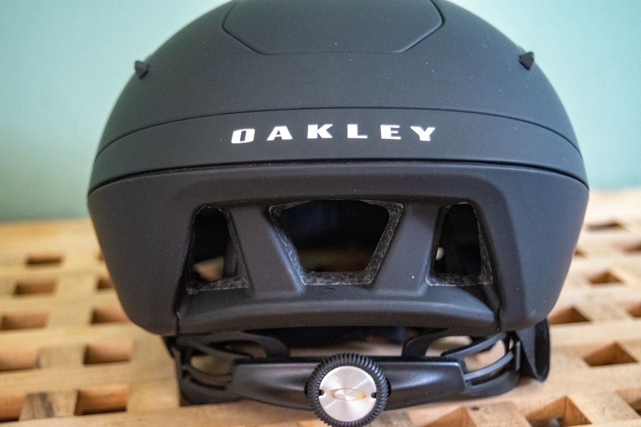 A rider wearing a black Oakley Velo Mac helmet in front of a green wall