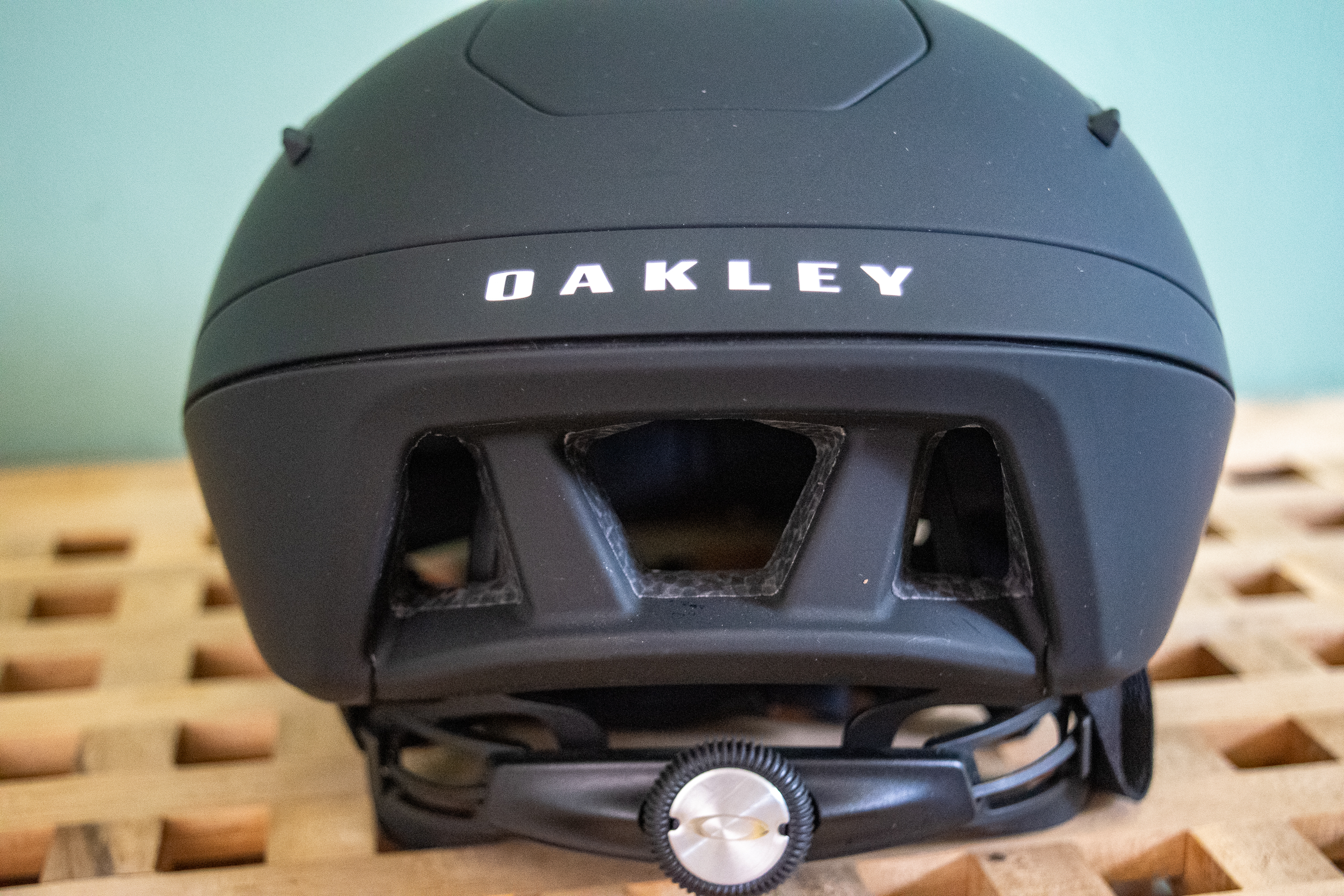 A rider wearing a black Oakley Velo Mac helmet in front of a green wall