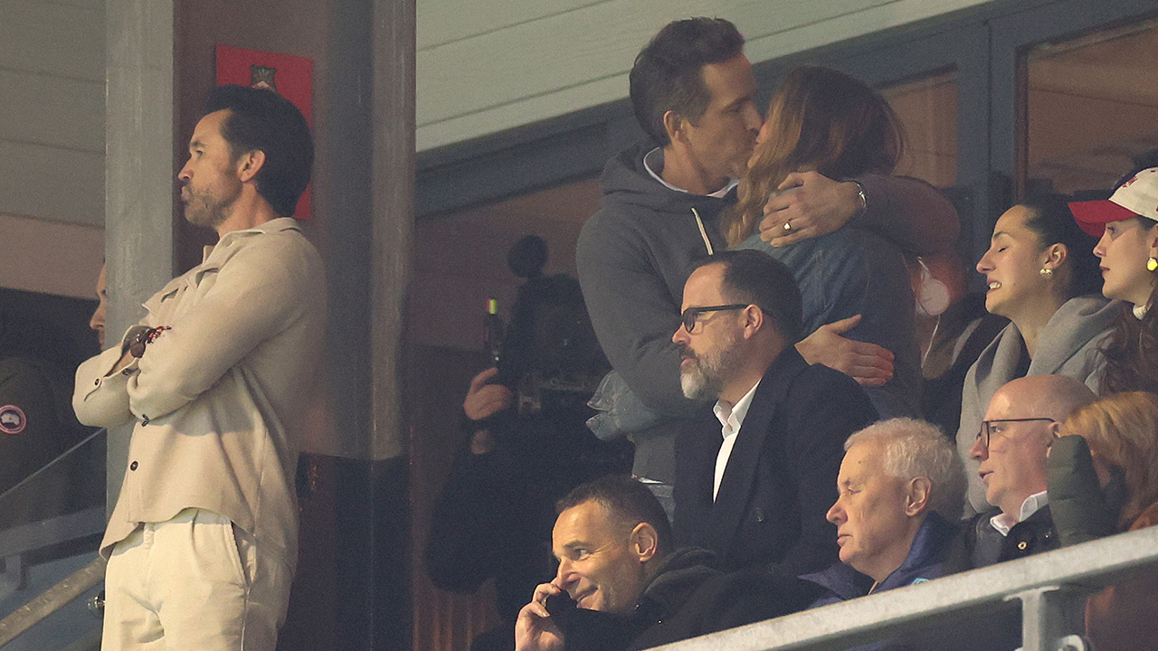 Ryan Reynolds kissing Blake Lively at a recent Wrexham game. They are standing in a box and Rob Mac is present.