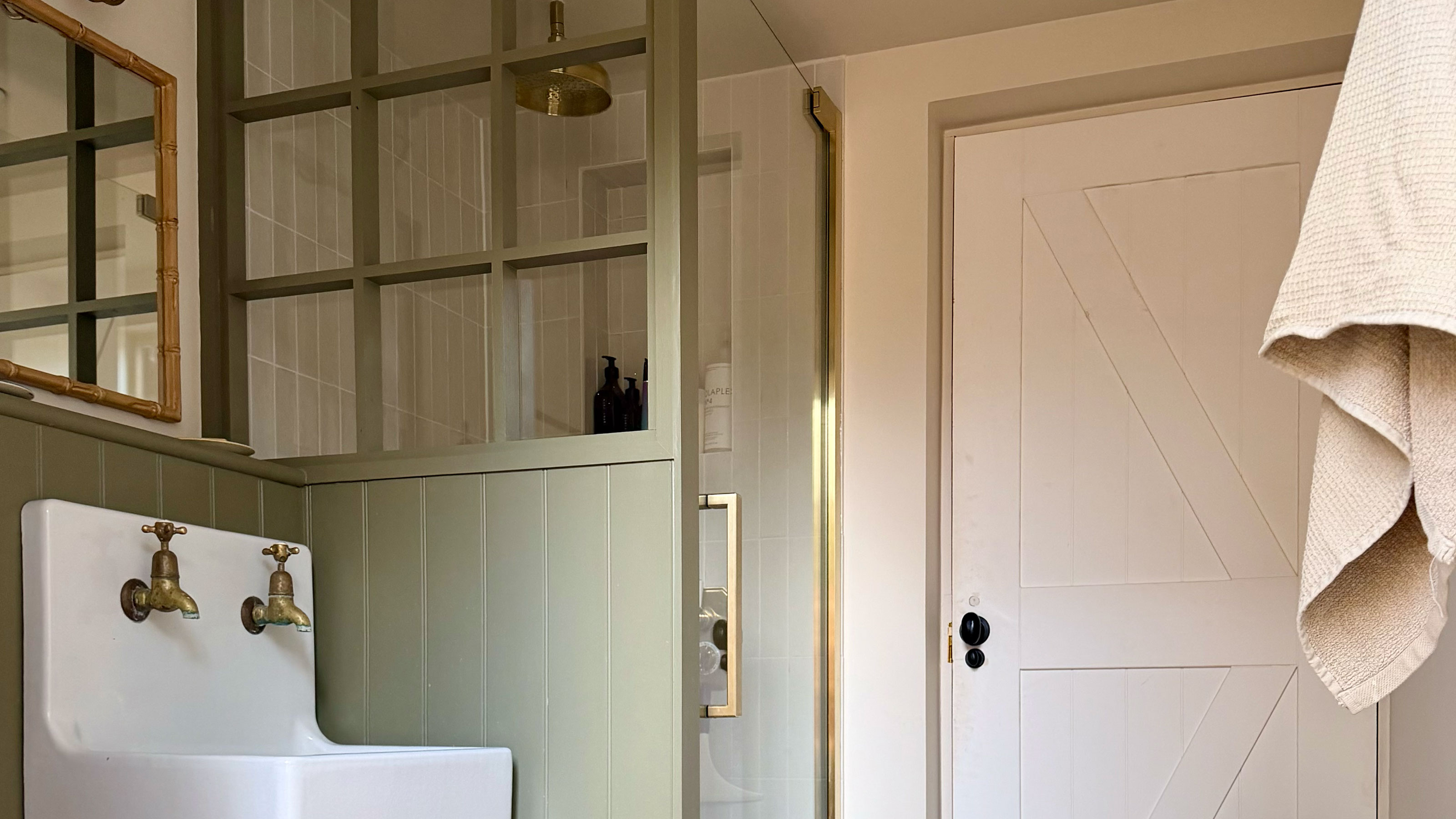 Cream bathroom with green wall panelling on wall and shower enclosure with glass front