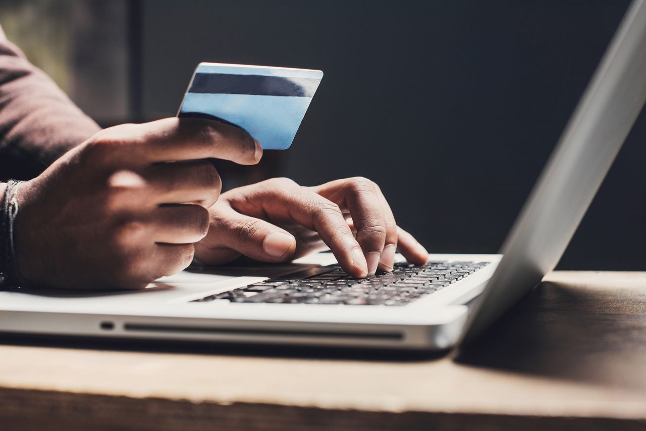 Investment scams represented by someone looking at a bank card while on their laptop