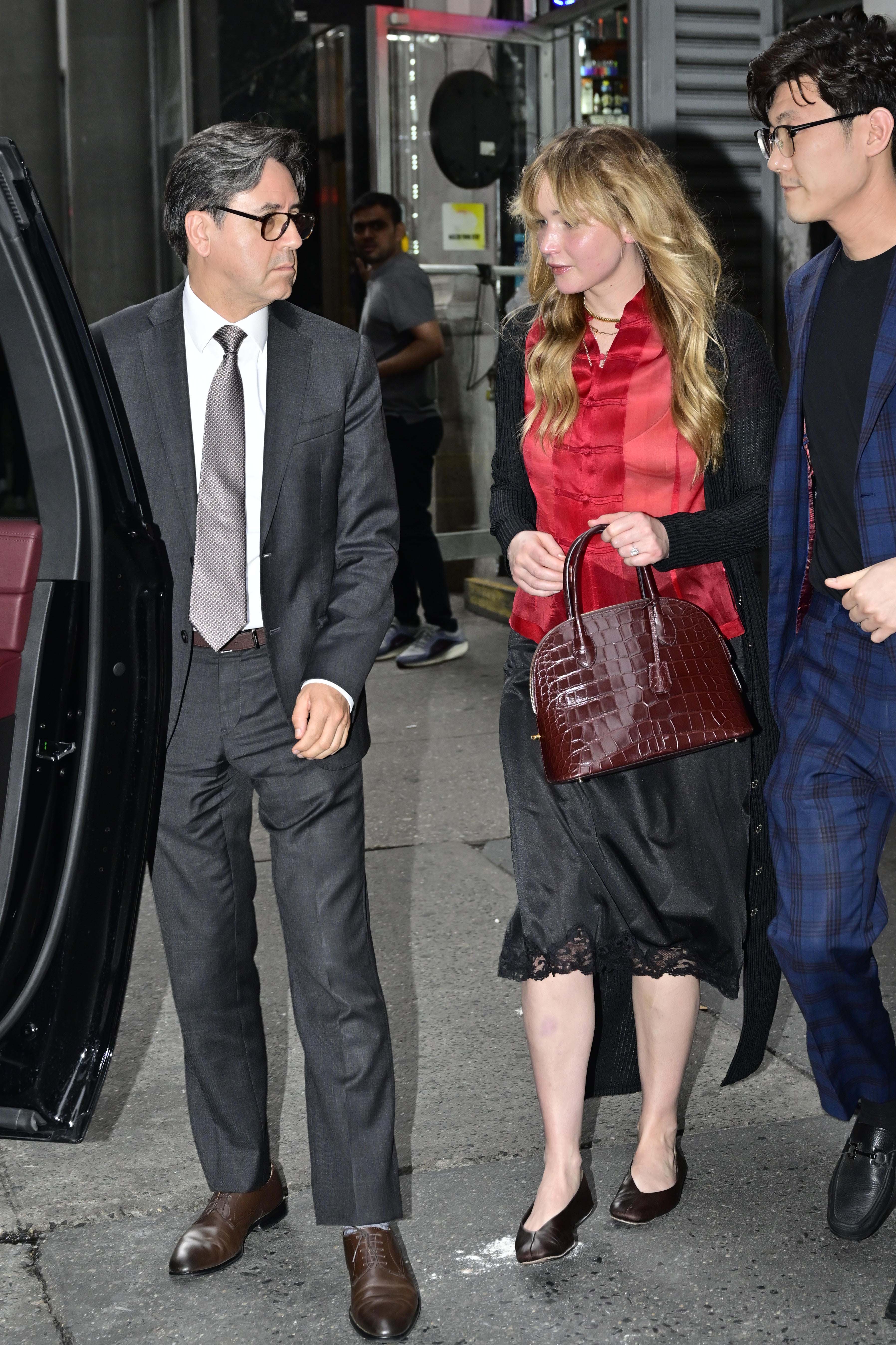 Jennifer Lawrence in NYC wearing a red top, black lace-trim skirt, flats, and carrying her The Row lady bag.