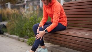 A runner with knee pain sits on a bench holding her knee