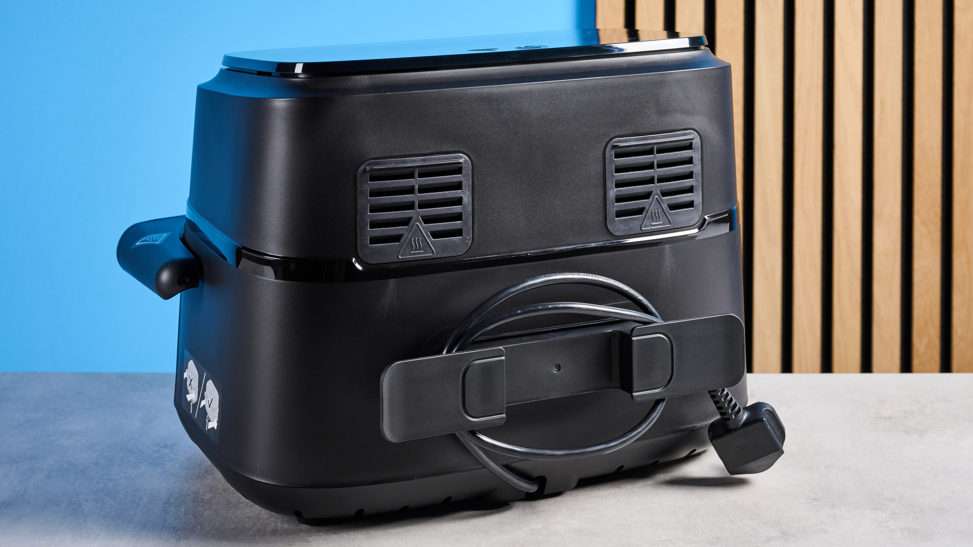 The cord storage of the Philips 1000 Series FlexDrawer Air Fryer photographed in front of a blue background.
