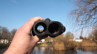 Kenko VC Smart Cellarto 10x30 WP binoculars held in a hand outside in front of a lake