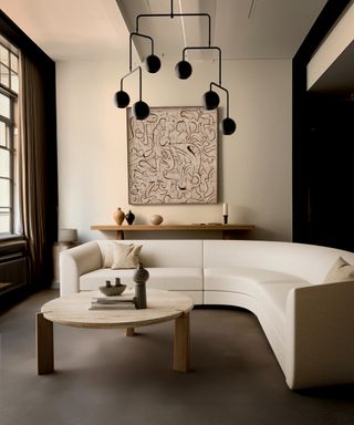 Living room with neutral curved sectional, coffee table, pendant light, console, artwork and pendant light