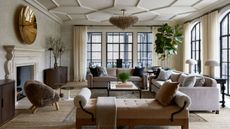 A large living room with decorative ceiling plaster, a neutral color palette, a wall of glass doors leading to a porch on two walls. Two taupe sofas with pillows and a beige chaise. 