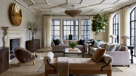 A large living room with decorative ceiling plaster, a neutral color palette, a wall of glass doors leading to a porch on two walls. Two taupe sofas with pillows and a beige chaise. 