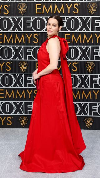 Emily Hampshire wearing a red gown with an open back