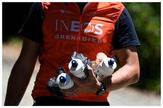 An Ineos Grenadiers soigneur holds water bottles and energy gels