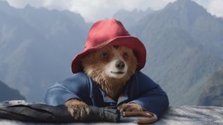 paddington bear in his blue coat and red hat with an umbrella at the top of a cliff in paddington in peru