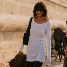 A woman in paris wears a white long-sleeve shirt with a black shoulder bag and black leggings.