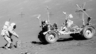 astronaut in a spacesuit squatting nearby a cylindrical-shaped experiment. to the right is the lunar rover. the scene is on the moon and cross shapes mark the image