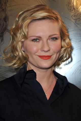 Kirsten Dunst with a curly bob hairstyle and a black top.