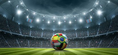 a picture of a soccer ball with different countries' flags sitting on a pitch in a soccer stadium 