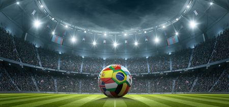 a picture of a soccer ball with different countries' flags sitting on a pitch in a soccer stadium 