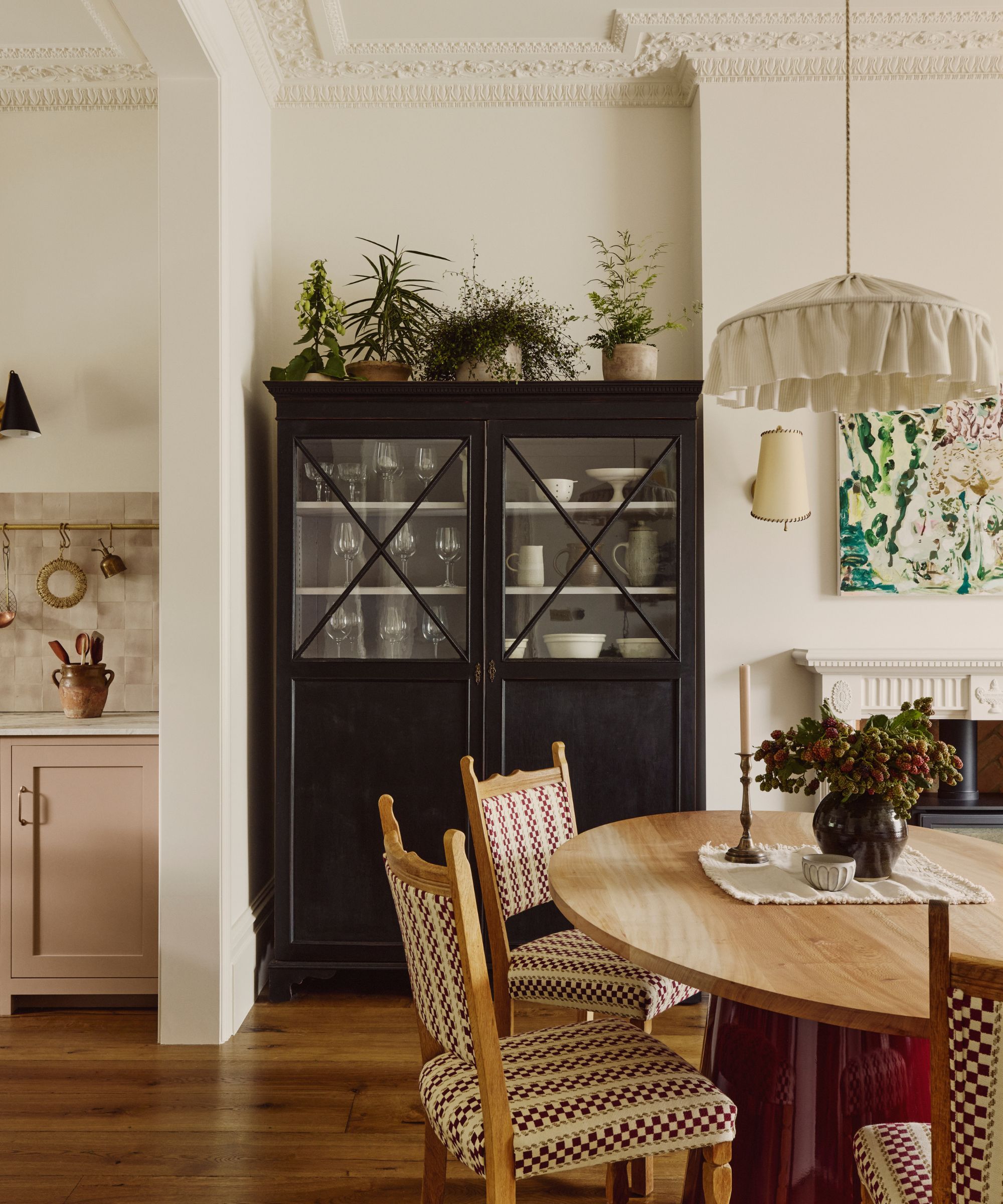 a dining room with a wood table, and wood chairs with patterned seats and backs, a large black storage cabinet with plants on top, and a pendant light with a fabric shade