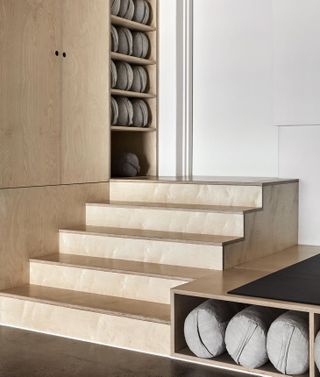 View of a wooden storage area with steps and white walls at Studio Warrior One. The storage unit is filled with grey bolster cushions