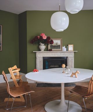 Sage green dining room walls with white ceiling, table and globe lights, wood and metal chairs, fireplace with flowers and art