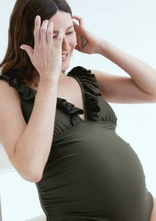 A pregnant model wearing a dark green maternity swimsuit from H&M. 