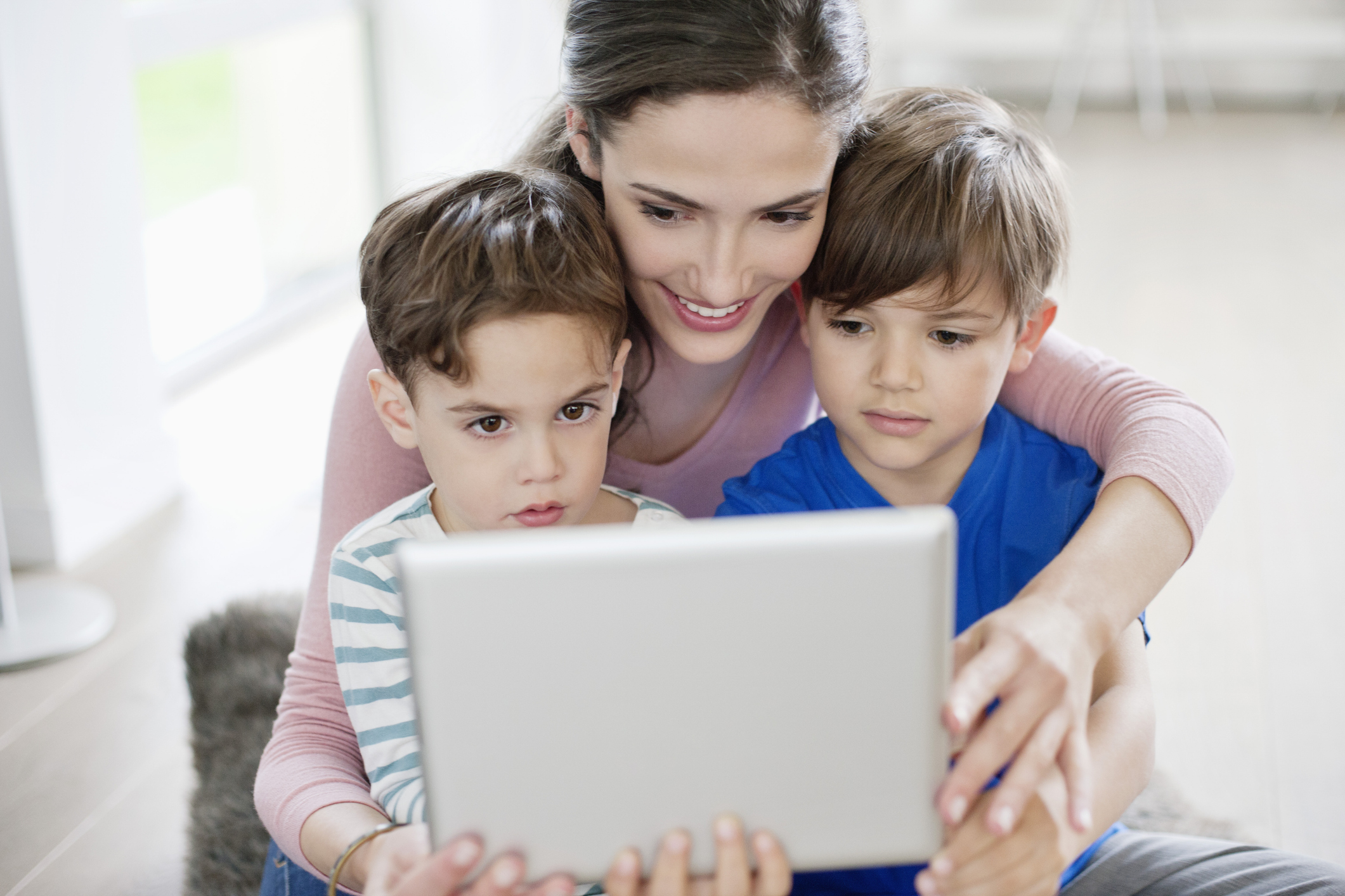 A mother and her two sons look at a tablet together.