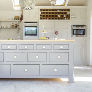 light grey island with multiple drawers, wooden worktop and grey cabinets