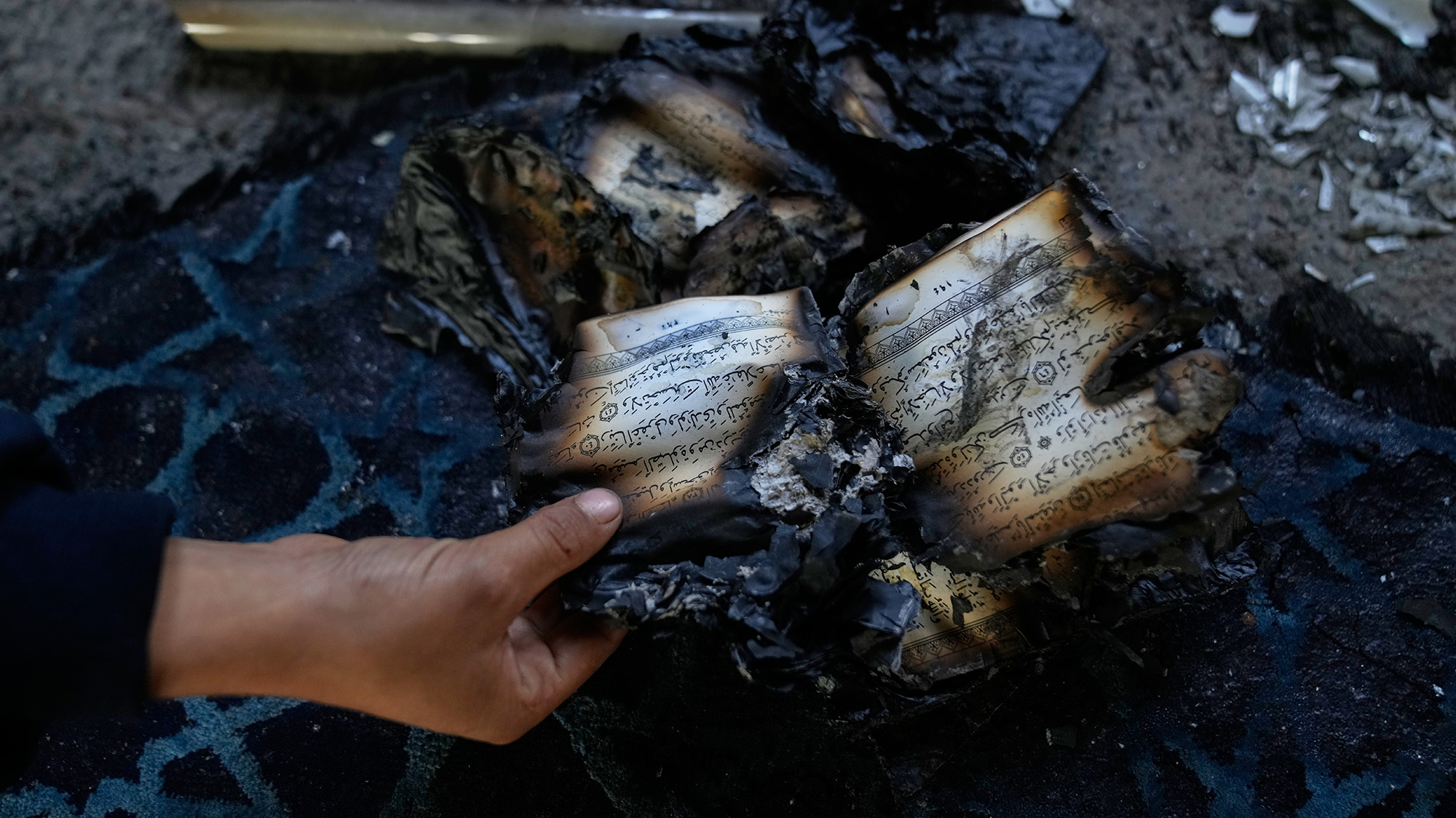 A boy inspects burnt copies of the Quran inside a mosque that was torched and defaced by Israeli settlers in the West Bank